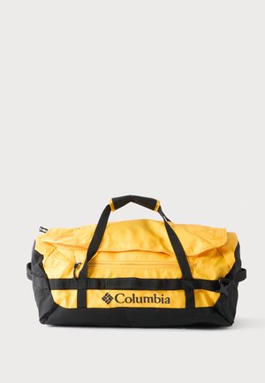 Bolsa de deporte tipo duffel Columbia amarilla y negra con cremallera y asas negras, descansando sobre una superficie blanca.