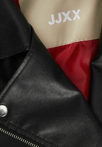 Veste en cuir noir avec une fermeture éclair argentée, un bouton-pression et une doublure beige et rouge avec le texte "JJXX." Texture lisse et design ajusté.