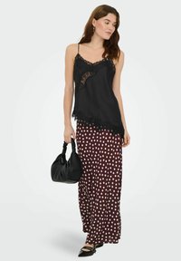 Czarna koszulka na ramiączkach z koronką w połączeniu z długą bordową spódnicą w grochy. Modelka trzyma czarną torebkę i nosi szpiczaste baleriny.