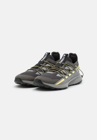 Scarpe da ginnastica grigie con tomaia testurizzata, dotate di accenti gialli, dettagli riflettenti e lacci elasticizzati per una vestibilità sicura.
