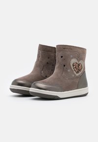 Pár hnědých semišových dětských bot s glitrovým srdíčkem a texturovanou gumovou podrážkou, umístěný na bílém pozadí.
