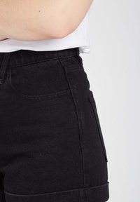 Shorts en denim noir avec une taille haute, des poches avant et un ourlet replié. Le tissu a une texture lisse et une légère élasticité.