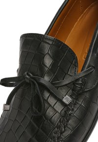 Schwarze Lederloafers mit einem strukturierten Krokodilmuster, ausgestattet mit einer Schnürung und silberfarbenen Hardware-Akzenten in der Nähe der Zunge. Braune Innenausstattung.