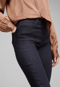 Vaqueros de mezclilla oscuros de talle alto con una textura suave, que cuentan con bolsillos laterales y sutiles costuras decorativas en la parte frontal.