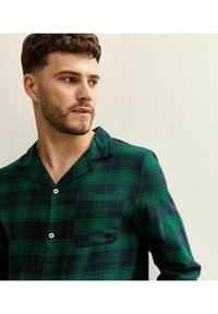 Camicia a quadri verde e blu navy in cotone, con colletto a punte, chiusura con bottoni, taschino e un tessuto morbido e strutturato.