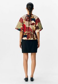 Short-sleeve, patterned blouse with a cinched waist and peplum design, paired with a fitted black skirt and flat black shoes.