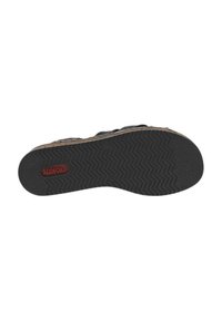 Semelle en caoutchouc noir avec un motif en zigzag, arborant un logo rouge. Le bord présente un accent beige, offrant un contraste avec l'ensemble du design.