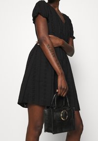 Svart kort klänning med puffärmar, med spetsliknande utskärningar och v-ringning. Matchad med en strukturerad svart handväska med cirkulär hårdvara.