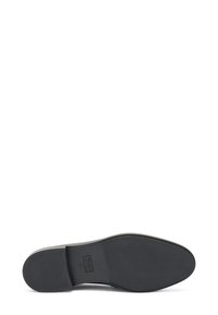 Suola di una scarpa elegante in pelle nera con grip testurizzato e logo del brand impressa vicino al tallone.