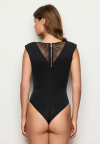 Black bodysuit with cap sleeves, lace detailing on the back, and a zipper closure at the neck. Smooth fabric and high-cut leg openings.