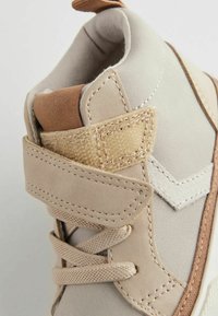 Beige hög sko med strukturerad yta, med brunt accent och krämfärgad sömnad. Inkluderar snören och ett kardborreband för stängning.