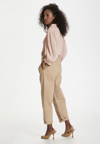 Blusa texturizzata rosa chiaro con maniche voluminose, abbinata a pantaloni beige a sigaretta e sandali con tacco color cuoio. Design minimalista.