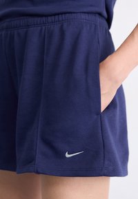 Calções azul-marinho feitos de tecido suave, com um cós elástico e bolsos laterais. Logotipo da Nike em prata na perna esquerda.