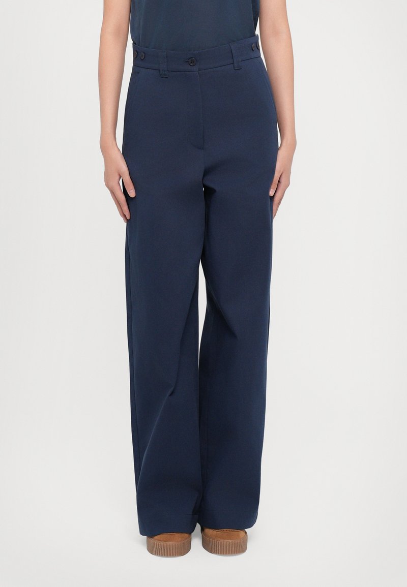 Pantaloni largi de culoare bleu marin, confecționați dintr-un material neted, cu închidere cu buton, buzunare laterale și croială dreaptă până la glezne.