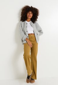 Chaqueta gris acolchada con cierres de botones, top corto blanco, pantalones anchos color mostaza y zapatos marrones con estampado de leopardo. Tejidos texturizados y corte relajado.