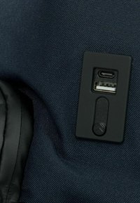 Tessuto blu navy con finitura testurizzata presenta un pannello nero contenente porte USB e USB-C e un pulsante con un accento triangolare.