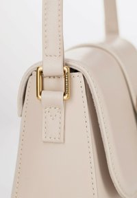 Borsa a mano in pelle beige con una forma strutturata, dotata di una fibbia in metallo dorato e dettagli di cucitura lungo la tracolla.