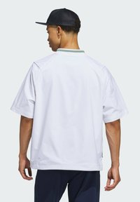 White short-sleeve shirt with a green-accented collar, made of lightweight material. Features a relaxed fit and back vent for breathability.
