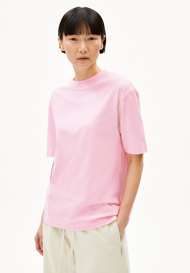 Roze katoenen t-shirt met korte mouwen en een ronde hals. Heeft een subtiele logo op de borst en is gecombineerd met lichtgekleurde broeken.