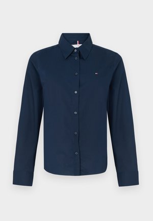 Mørkeblå langermet skjorte med knapper laget av glatt stoff. Har krage, frontknapper og en liten logo på venstre bryst.