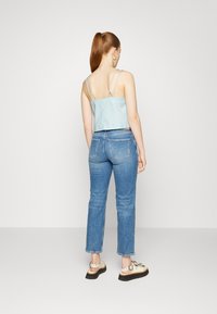 Top cropped azul claro, com padrão e alças finas, combinado com calças de ganga azuis de perna reta e cintura alta. Costas fechadas e calçado casual com adornos.