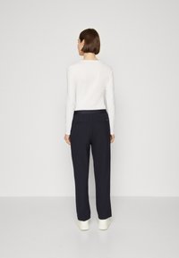 Top bianco a maniche lunghe abbinato a pantaloni blu navy con taglio dritto, cintura elastica e due tasche posteriori. Tessuto morbido.