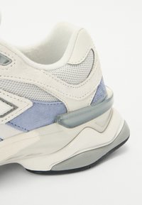 White and light blue sneaker with mesh and suede materials; features a cushioned sole, rounded shape, and translucent accents.