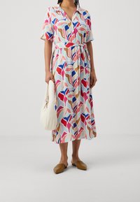 Krátký rukáv, šaty po kolena z lehkého materiálu s abstraktním, barevným listovým vzorem. Obsahuje pás s opaskem. Nosen�é s plochými botami a bílou taškou.