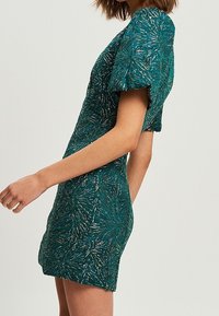 Vestido verde con estampado, mangas abullonadas, silueta ajustada y tejido texturizado que presenta acentos de color claro formando un diseño floral.