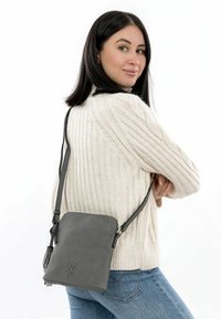 Grå tekstureret crossbody taske med lynlåslukning og en lang rem, der har et diskret præget logo. Tasken har en rektangulær form.