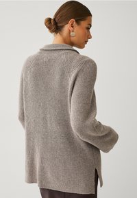 Grå strikket cardigan med sjalskrave, lange ærmer, sideslidser og en tekstureret overflade. Stoffet ser blødt og varmt ud.