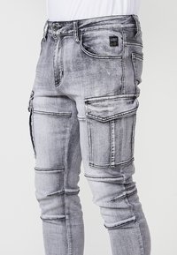 Grijze denim cargo broeken met meerdere zakken, gedetailleerde stiksels en een slank gesneden ontwerp. Kenmerken een vervaagde wassing en ritsaccenten.