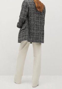 Blazer long à carreaux noir et blanc, coupe ample, assorti à un pantalon droit beige clair. La texture semble tissée et douce.