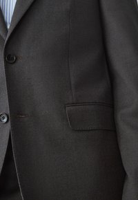 Dunkelgrauer strukturierter Blazer mit einem Reverskragen, zwei Knöpfen, einer Brusttasche und subtilen Stitching-Details. Geeignet für formelle Anlässe.