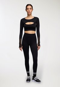 Completo sportivo nero composto da un top a maniche lunghe con ritagli e inserti in rete, abbinato a legging a vita alta e sneakers nere.