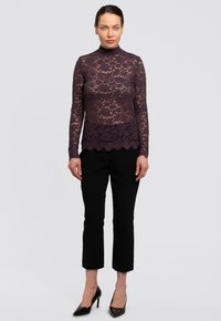 Lace lange mouw top in dieppaars met hoge hals en scalloped zoom, gedragen met zwarte cropped broek en zwarte hakken.