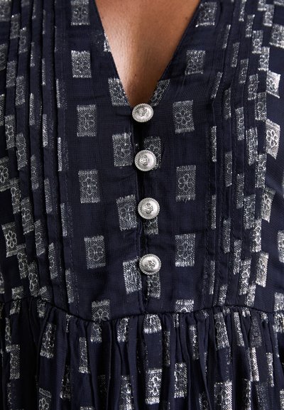Marineblaues Kleid mit silbernem geometrischem Muster, plissierter Textur, V-Ausschnitt und fünf dekorativen Knöpfen an der Brust.