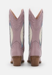 Liliowe kowbojki z wydłużonymi cholewkami, niebieskimi i kremowymi akcentami, złożonym haftem i drewnianymi obcasami. Gładka skórzana faktura.