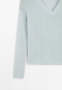 Maglione azzurro chiaro con scollo a V realizzato in morbido tessuto a maglia testurizzato. Caratterizzato da maniche lunghe e orlo a coste. Assenza di motivi o elementi metallici visibili.