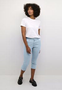 Ljusblå capribyxor i stretchigt material, som kombineras med en åtsittande vit t-shirt och svarta loafers, med en enkel design och ankellängd.