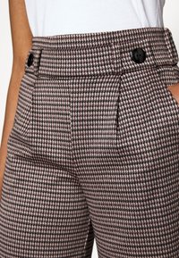 Rutig högmidjade byxor i vinröd, svart och krämfärgad. Har två framfickor och en dubbelknäppning med en mjuk textur.