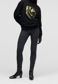 Felpa nera con grafica metallica, abbinata a jeans skinny scuri con motivo e stivaletti neri con tacco a blocco.