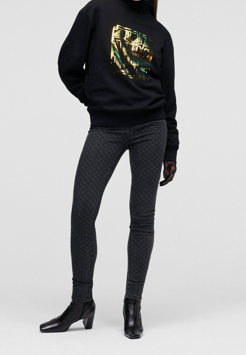 Felpa nera con grafica metallica, abbinata a jeans skinny scuri con motivo e stivaletti neri con tacco a blocco.