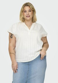 Blusa blanca de manga corta con rayas verticales naranjas, con escote en forma de V y un corte holgado, combinada con una falda de mezclilla.