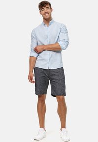 Chemise à rayures bleu clair à boutons, associée à un short gris foncé. Les accessoires comprennent des baskets blanches. Le tissu semble texturé et décontracté.