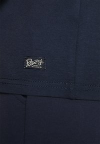 Mörkblå bomullstyg med en strukturerad yta. Har en liten rektangulär svart etikett med vit text, sydd vid fållen.