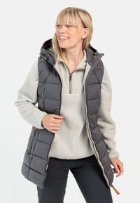 Grå quiltet puffer vest med hætte, med lynlås og snøre. Parret med en lys grå fleecepullover, begge er bløde i teksturen.