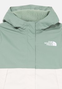 Veste vert clair et blanche avec une capuche en polaire douce, un tissu extérieur lisse et le logo The North Face sur la poitrine.