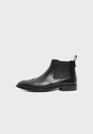 Black leather Chelsea ankle boot with elastic side panels and pull tab, featuring a low heel and rounded toe.