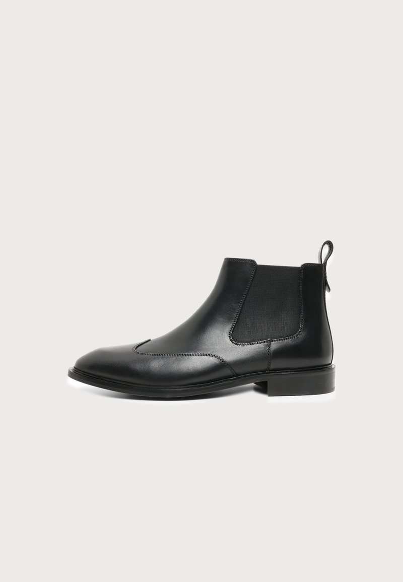 Bottine Chelsea en cuir noir avec panneaux latéraux élastiques et languette, dotée d'un talon bas et d'un bout arrondi.
